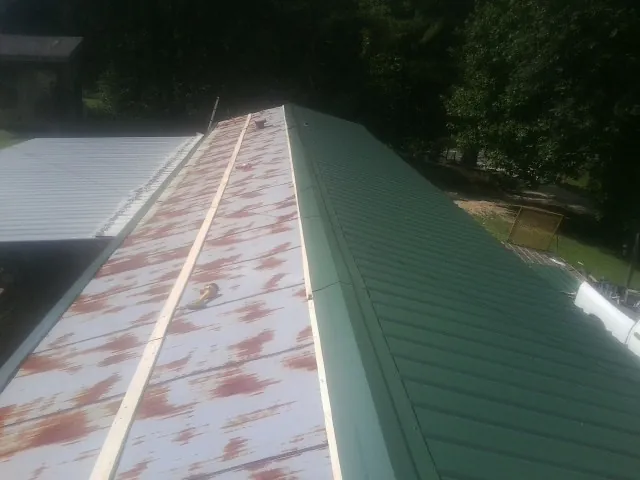 Old rusted panels beside newly installed green metal roofing — Wind Damage Roof Repair by Roofing Brothers in Millerton