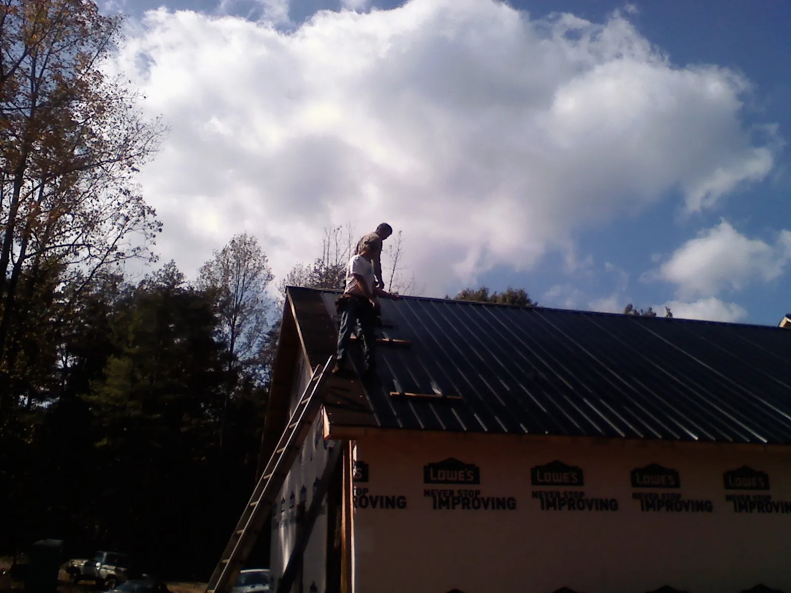 Roofer fastening dark metal panels high against a cloudy sky, from a Roof Inspection job in Millerton